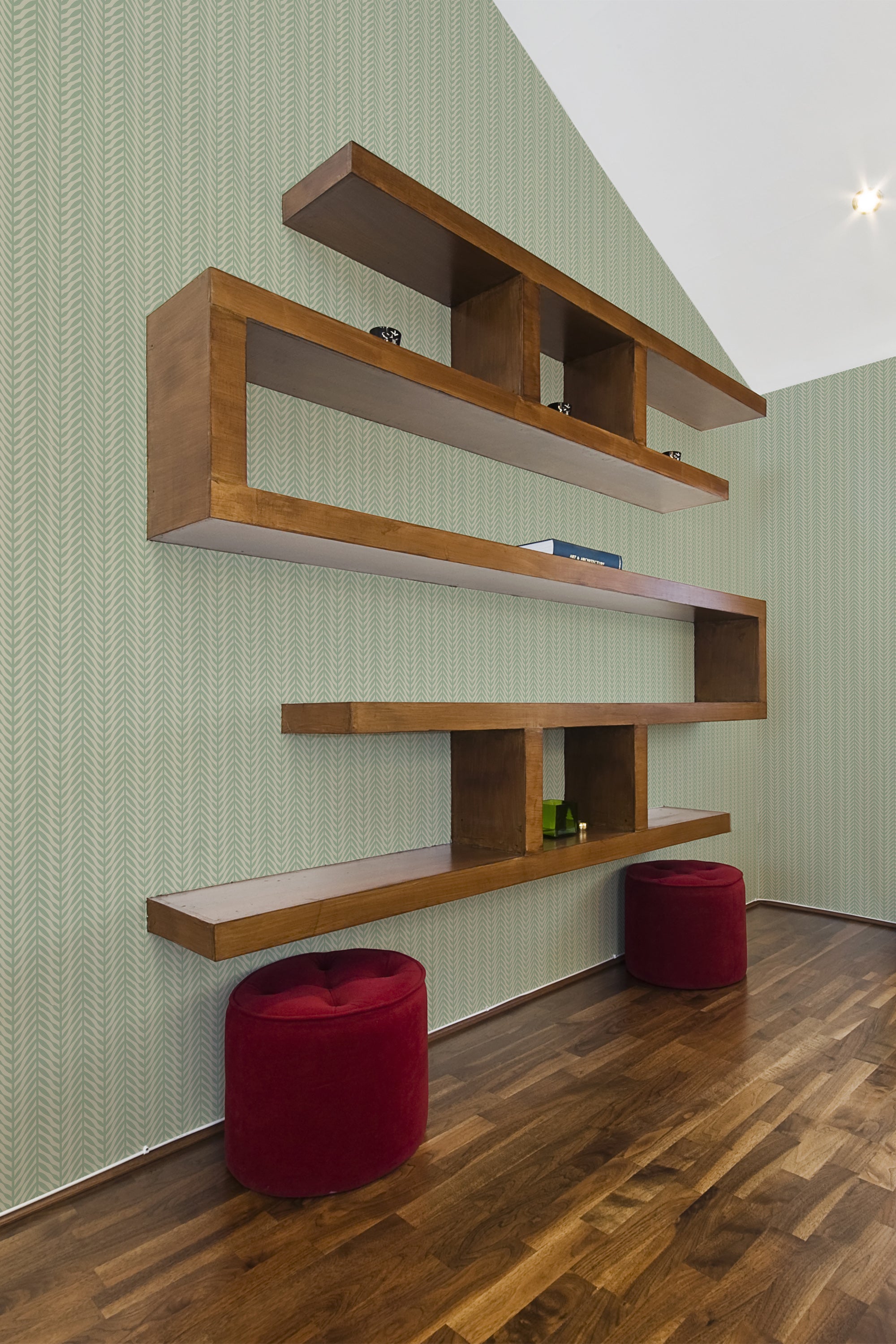 A room with Green Herringbone pattern wallpaper with interlocking zigzag lines, complemented by wooden shelves and two red stools, traditional wallpaper.