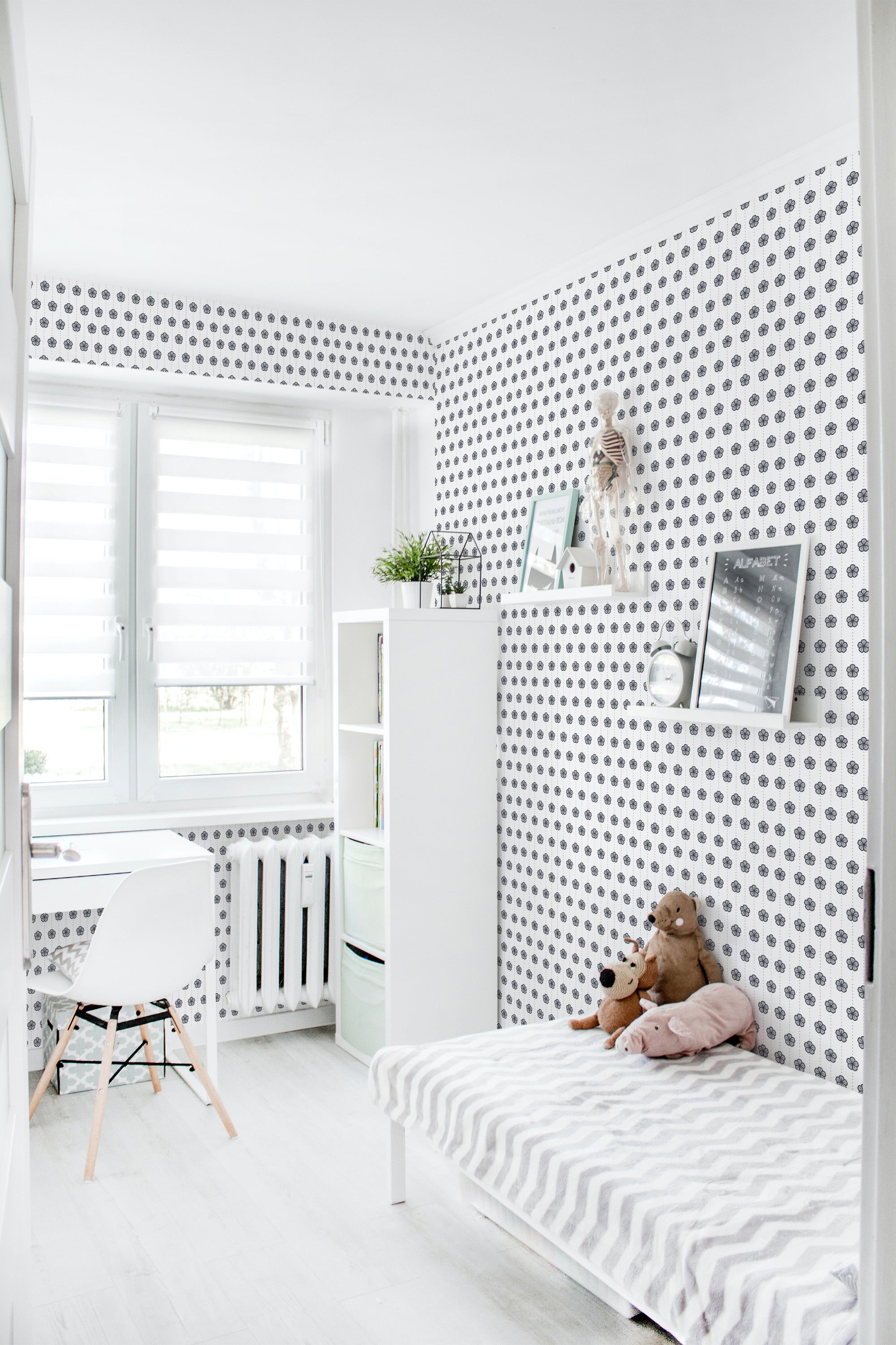 A room with wallpaper adorned with a repeating pattern of Japanese flowers, creating a serene ambiance. The design includes small, detailed floral motifs in dark tones on a light background, complementing the room's minimalist decor. A white bed, chair, and shelving unit blend seamlessly with the soft colors of the wallpaper, creating a tranquil and balanced atmosphere. Traditional wallpaper.