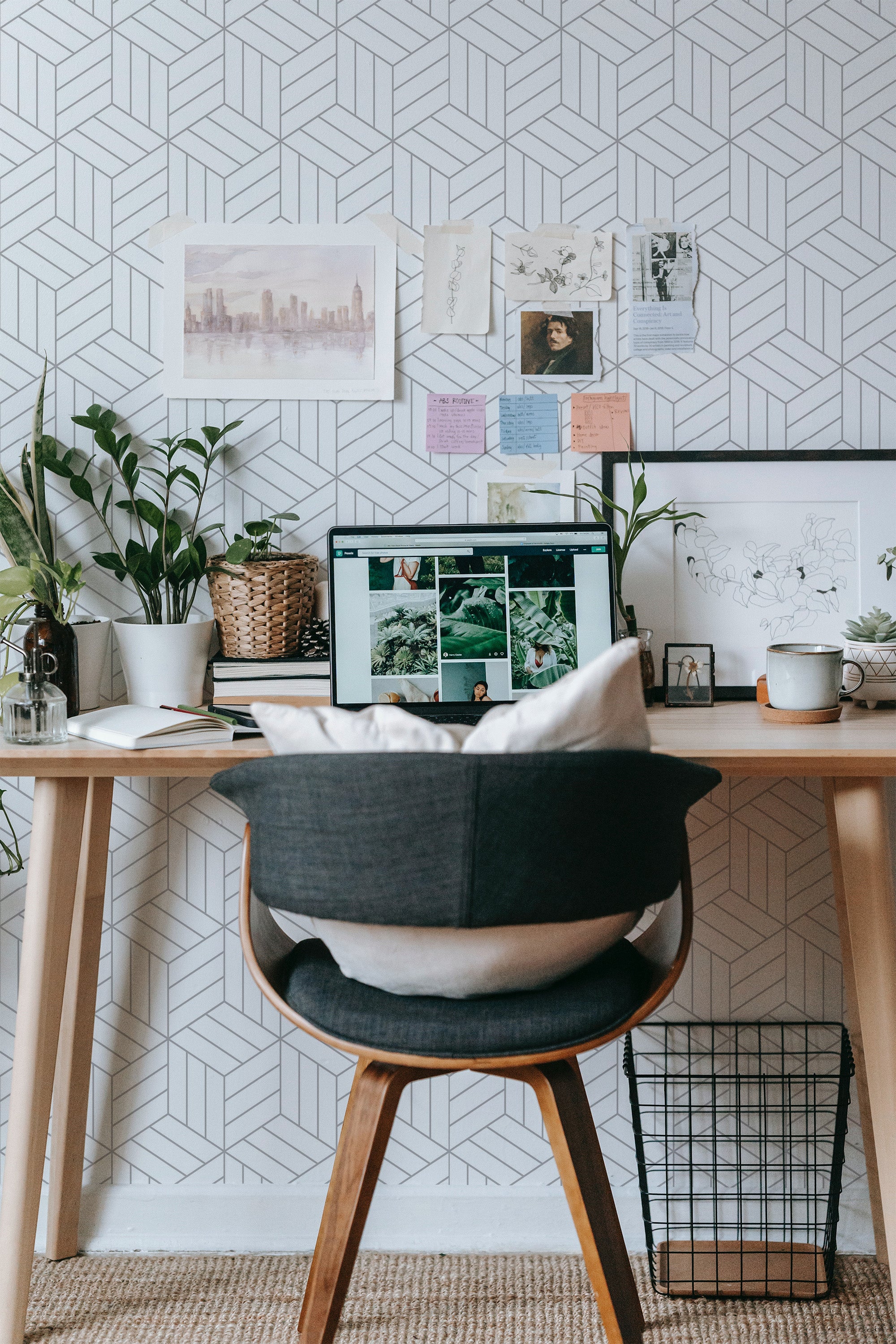 Self-adhesive geometric hexagon wallpaper with a minimalist, modern design in a light color scheme applied on a room wall, adding a contemporary touch to the workspace setup with plants, art, a desk, and a chair.