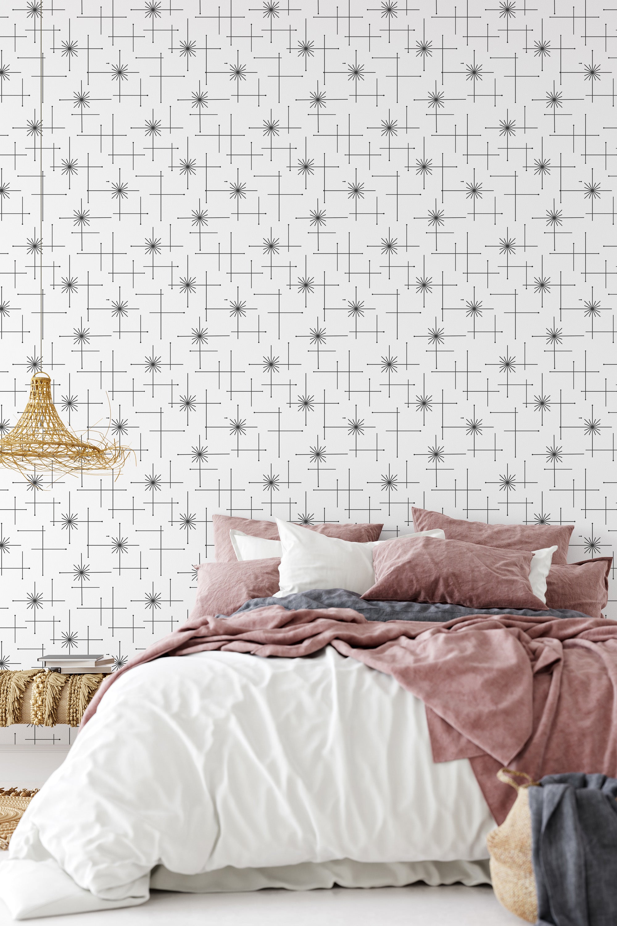 A bedroom with a wall covered in white wallpaper with a black seamless stars pattern, behind a bed with pink and white bedding, ending with traditional wallpaper.