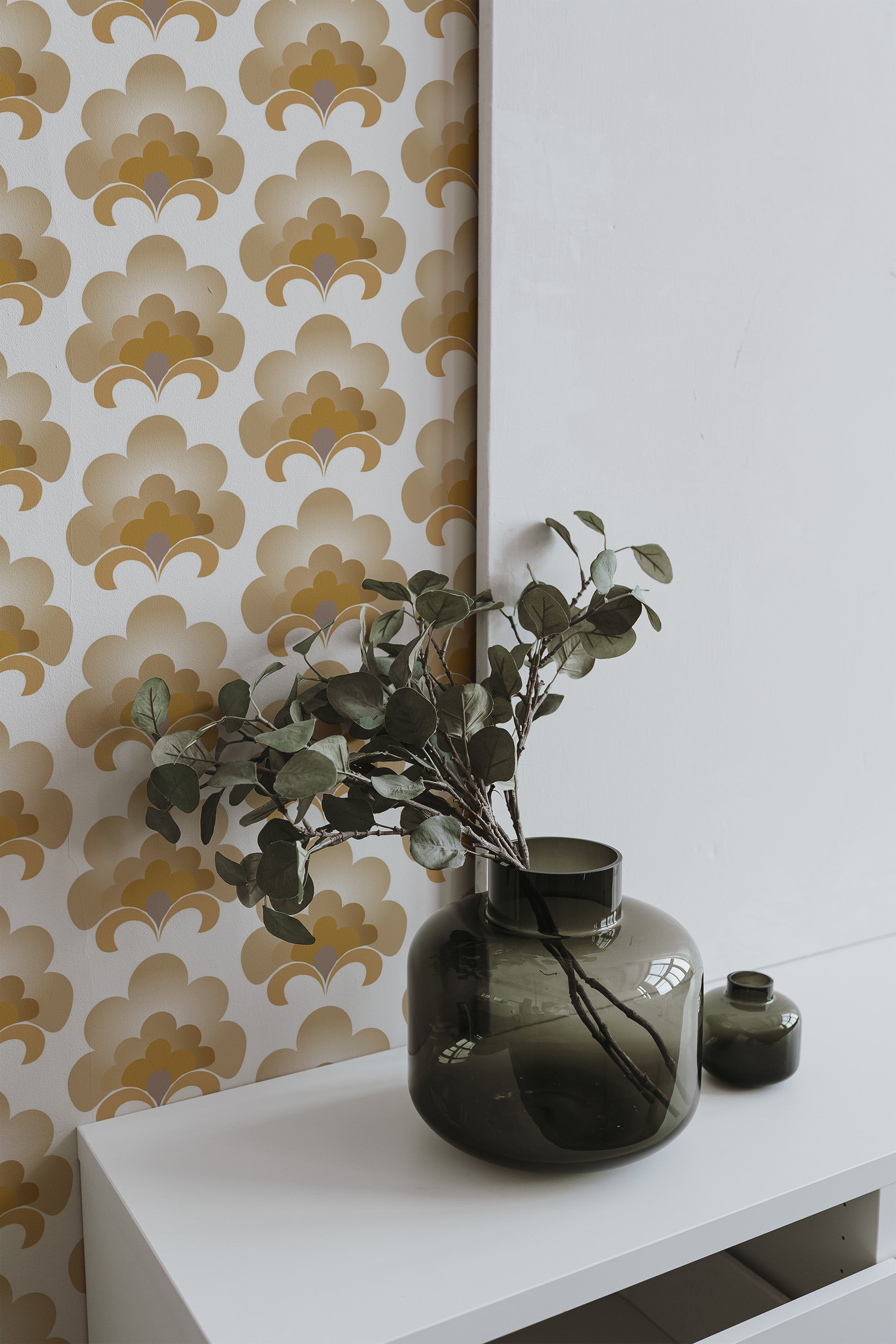 Self-adhesive vintage wallpaper with a retro geometric pattern in muted gold and beige tones, complementing the modern minimalist decor with a dark green glass vase filled with eucalyptus branches.