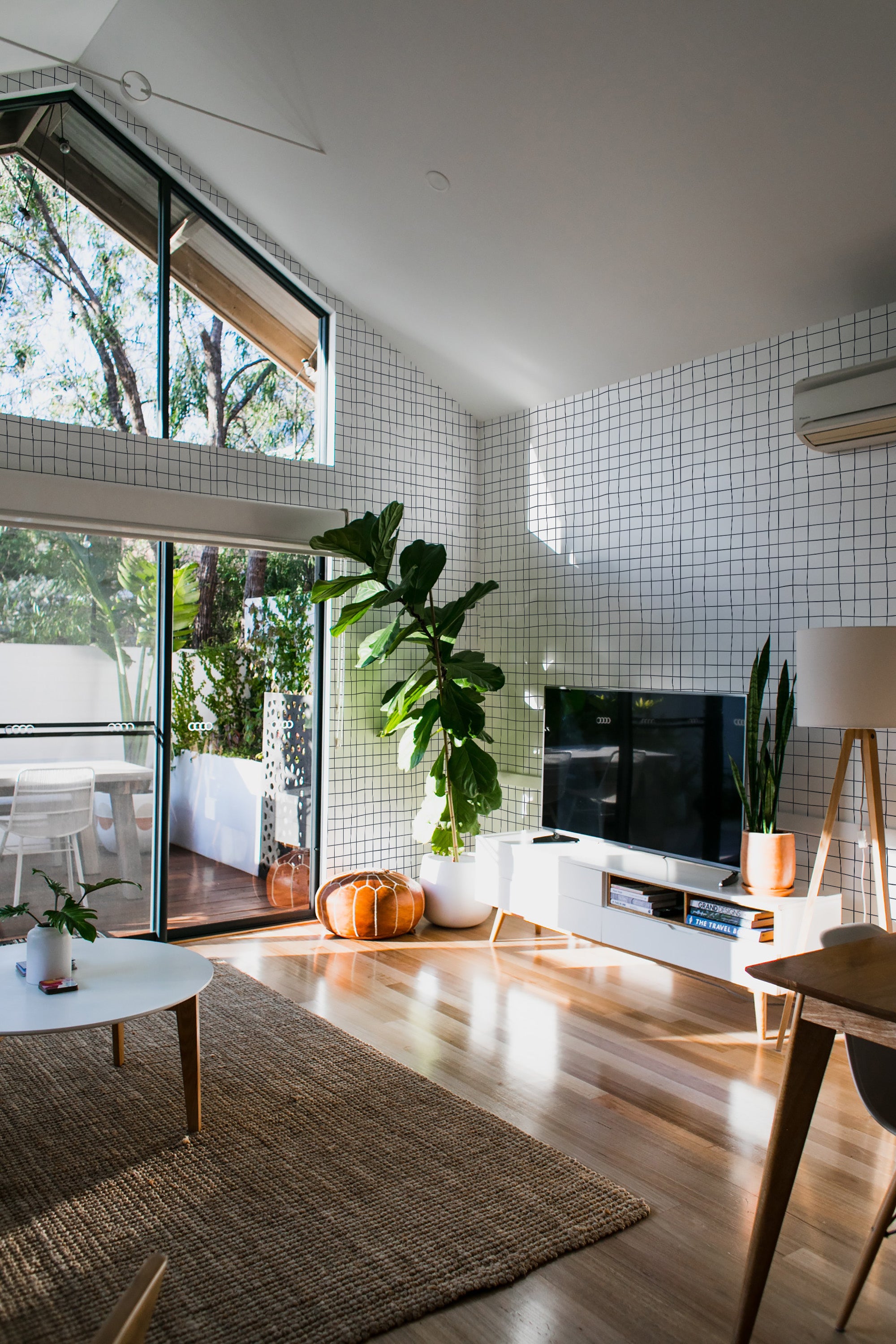 A room with walls covered in a wallpaper design of an uneven grid pattern with irregularly spaced thin black lines over a white background, giving a subtle geometric look. The grid lines create an abstract, modern feel, enhancing the natural light in the space. Traditional wallpaper.