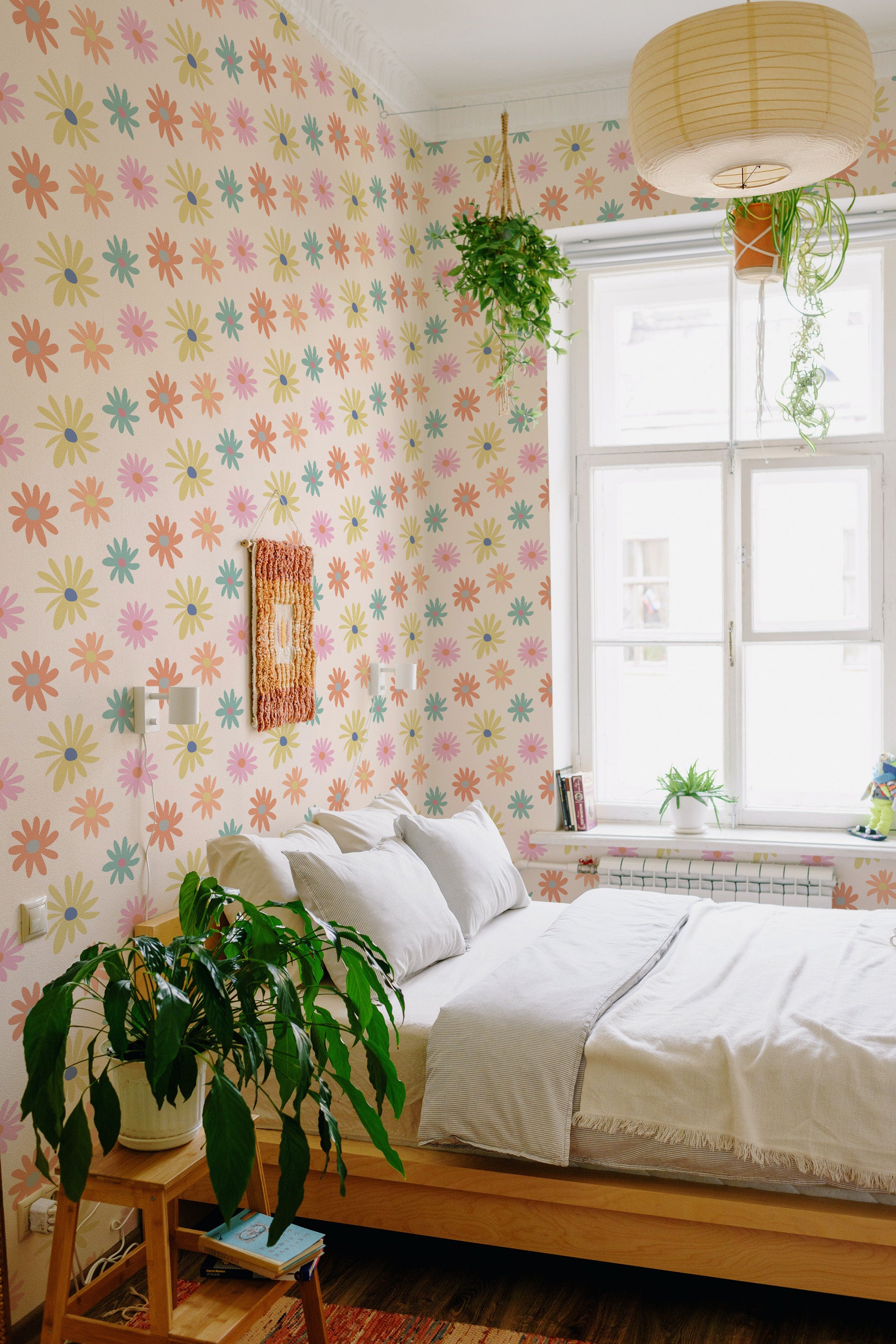 The wallpaper has a colorful retro floral pattern with daisy-like flowers in pastel shades of pink, yellow, blue, and white on a beige background. The pattern creates a lively and vintage ambiance, adding warmth and character to the room. Traditional wallpaper.