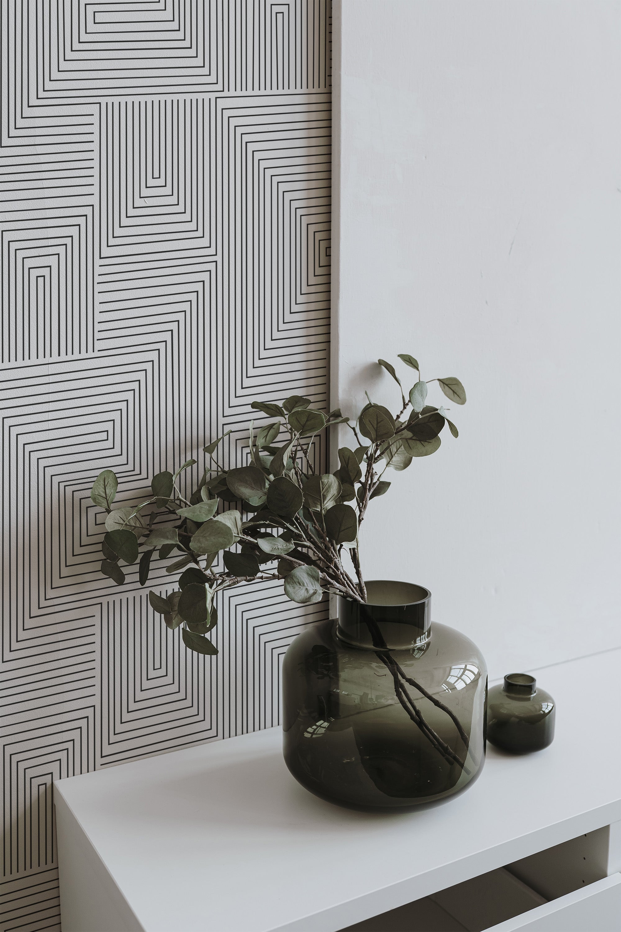Self-adhesive wallpaper with a geometric pattern of intricate, black lines forming concentric rectangles on a white background.