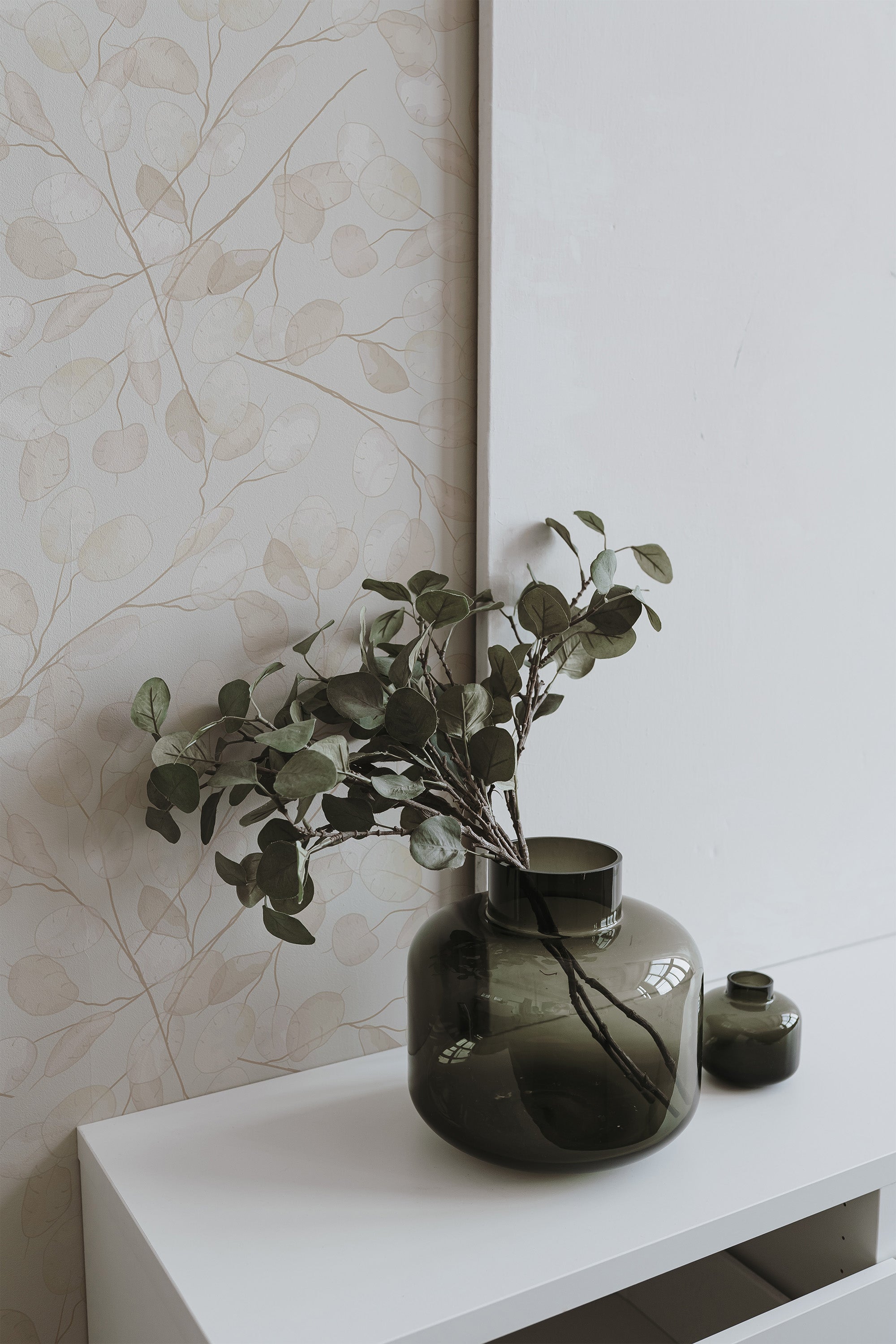 Self-adhesive wallpaper with a subtle gradient leaf pattern on a light background, complemented by green vases with foliage.