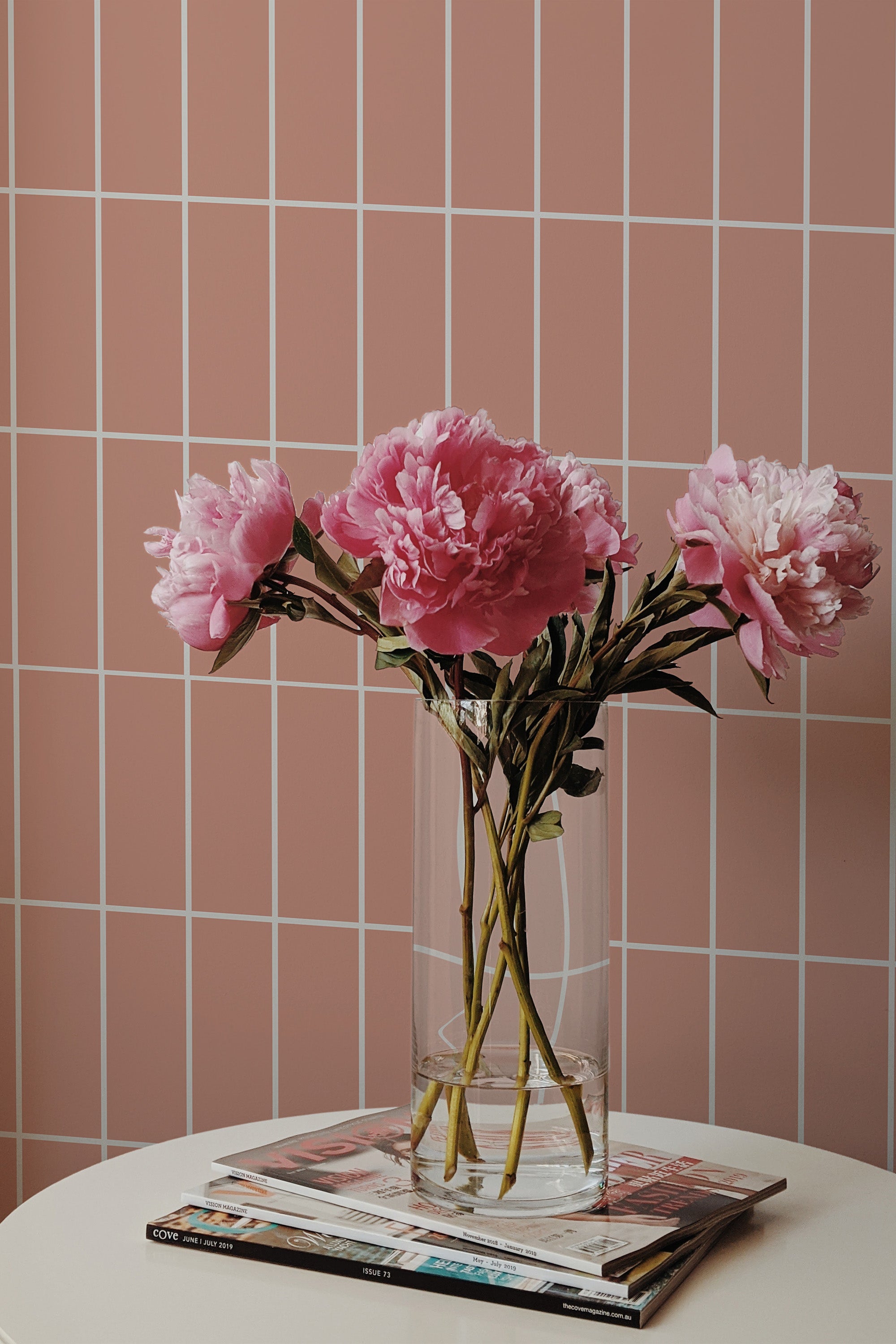 Self-adhesive pink tile-patterned wallpaper with lines creating a grid design on a wall, complemented by a bouquet of pink flowers on a table.