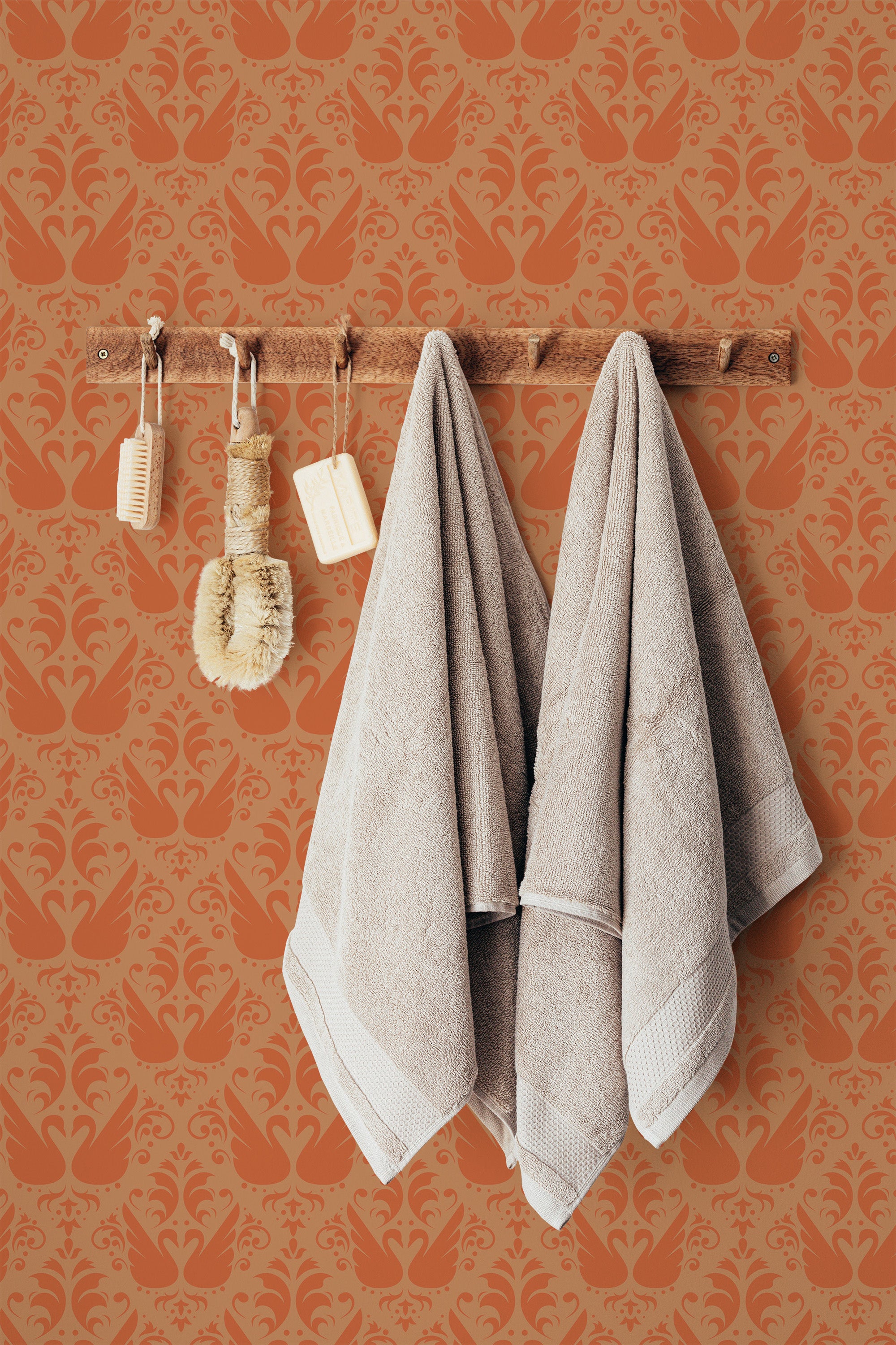 Self-adhesive wallpaper with an orange swan pattern on a wall, complemented by hanging soft towels and wooden bathroom accessories.