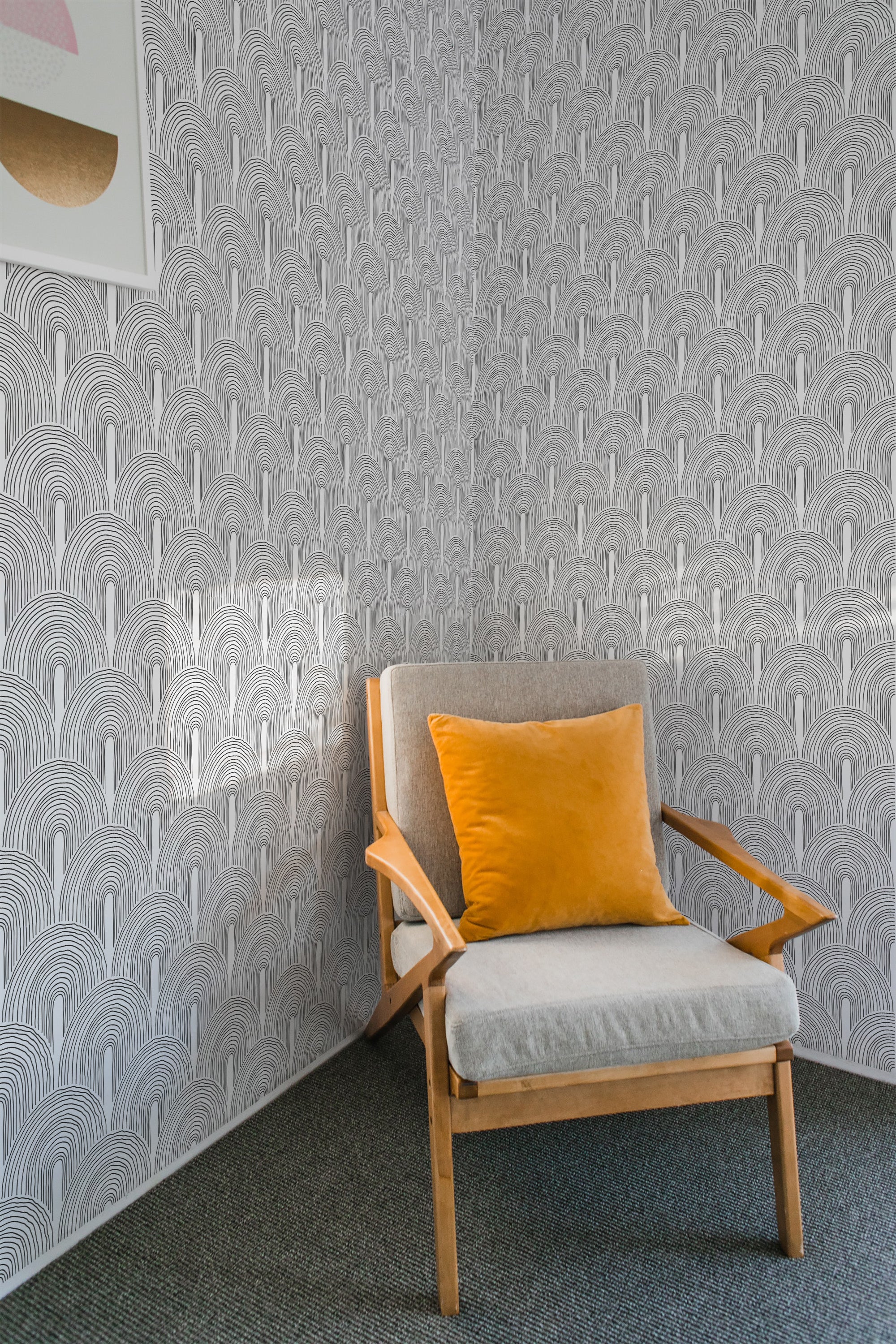 A room with art deco line arch wallpaper, featuring a repetitive pattern of arching lines in black and white, creating a vintage geometric aesthetic. A beige armchair with a mustard yellow pillow is placed against the wall, giving the space a cozy atmosphere with traditional wallpaper.