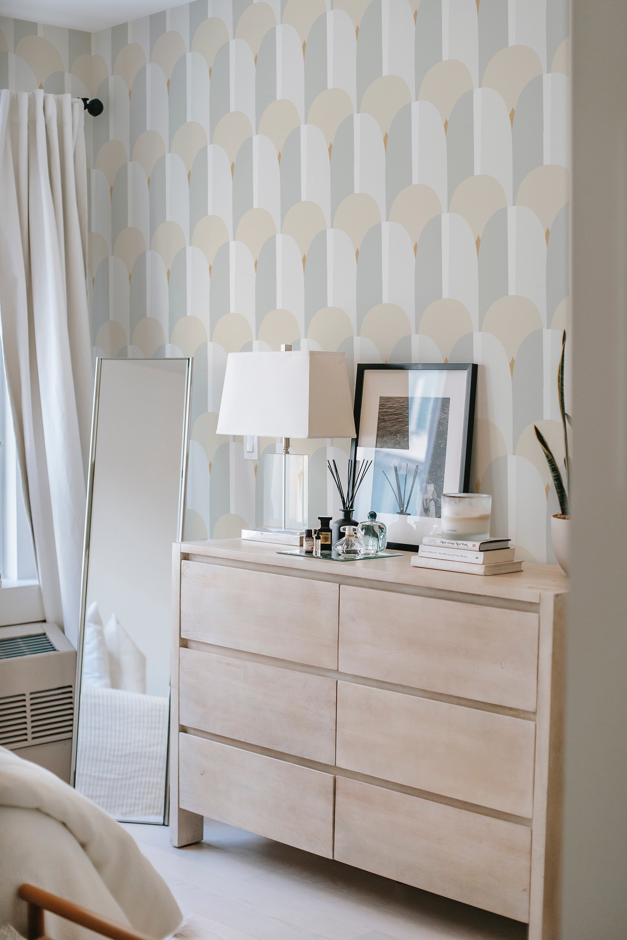 A serene room with a chest of drawers against a wall covered in Pastel Art Deco wallpaper, with scalloped patterns in soft, muted colors, reflecting a traditional wallpaper style.