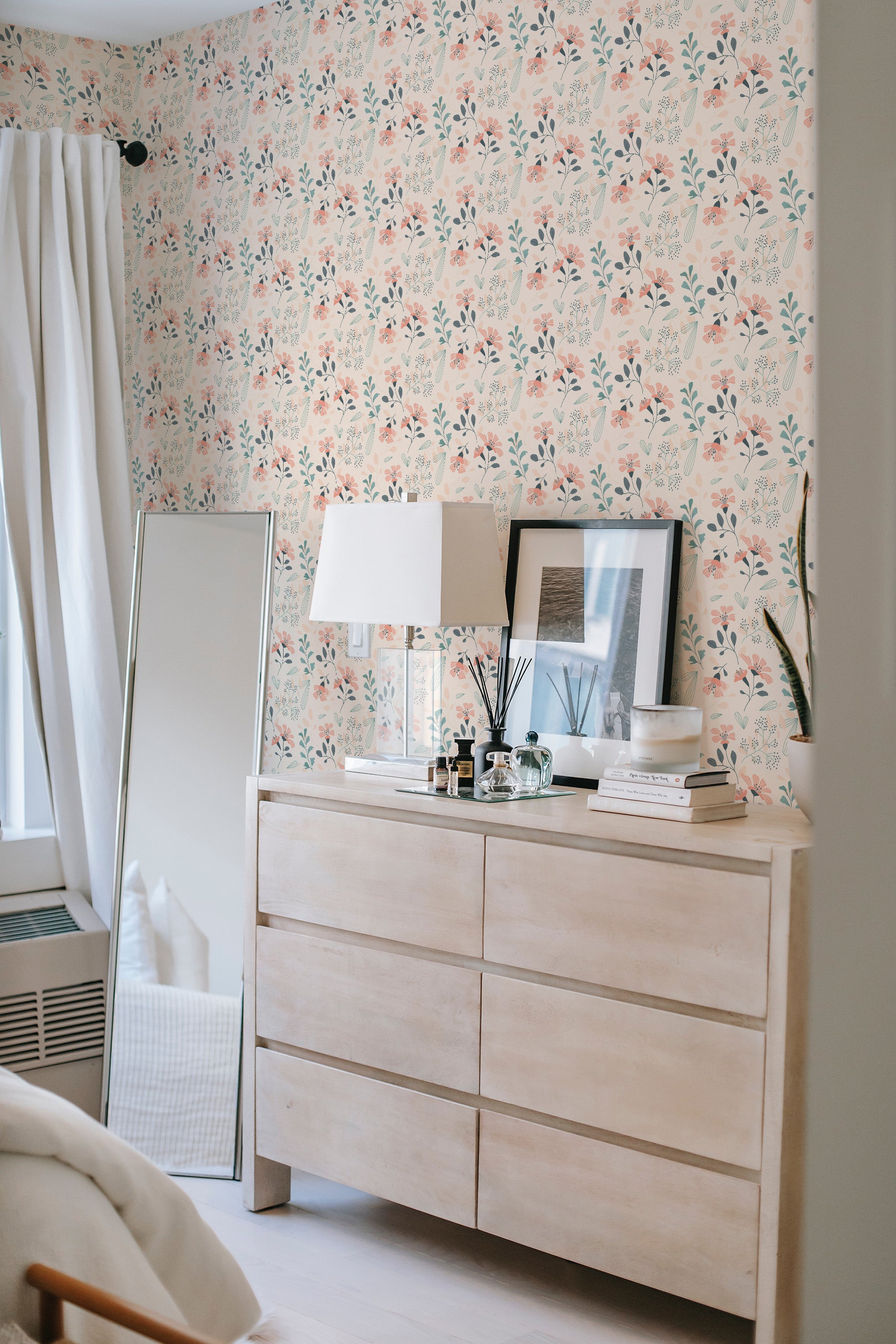 Self-adhesive pastel pink floral wallpaper with subtle pink flowers and green leaves, creating a soft and refreshing garden-like pattern on the brightly lit wall behind a light wood dresser.