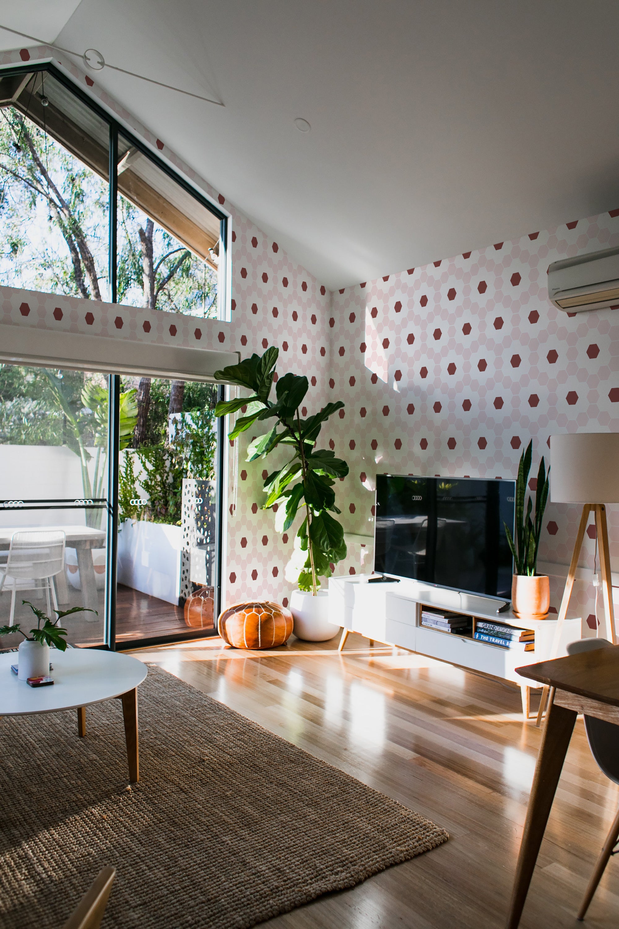 A living room with walls adorned in geometric floral tile wallpaper, featuring a repeating pattern of pinkish hexagons resembling flowers on a white background, adding a subtle and traditional touch to the space.