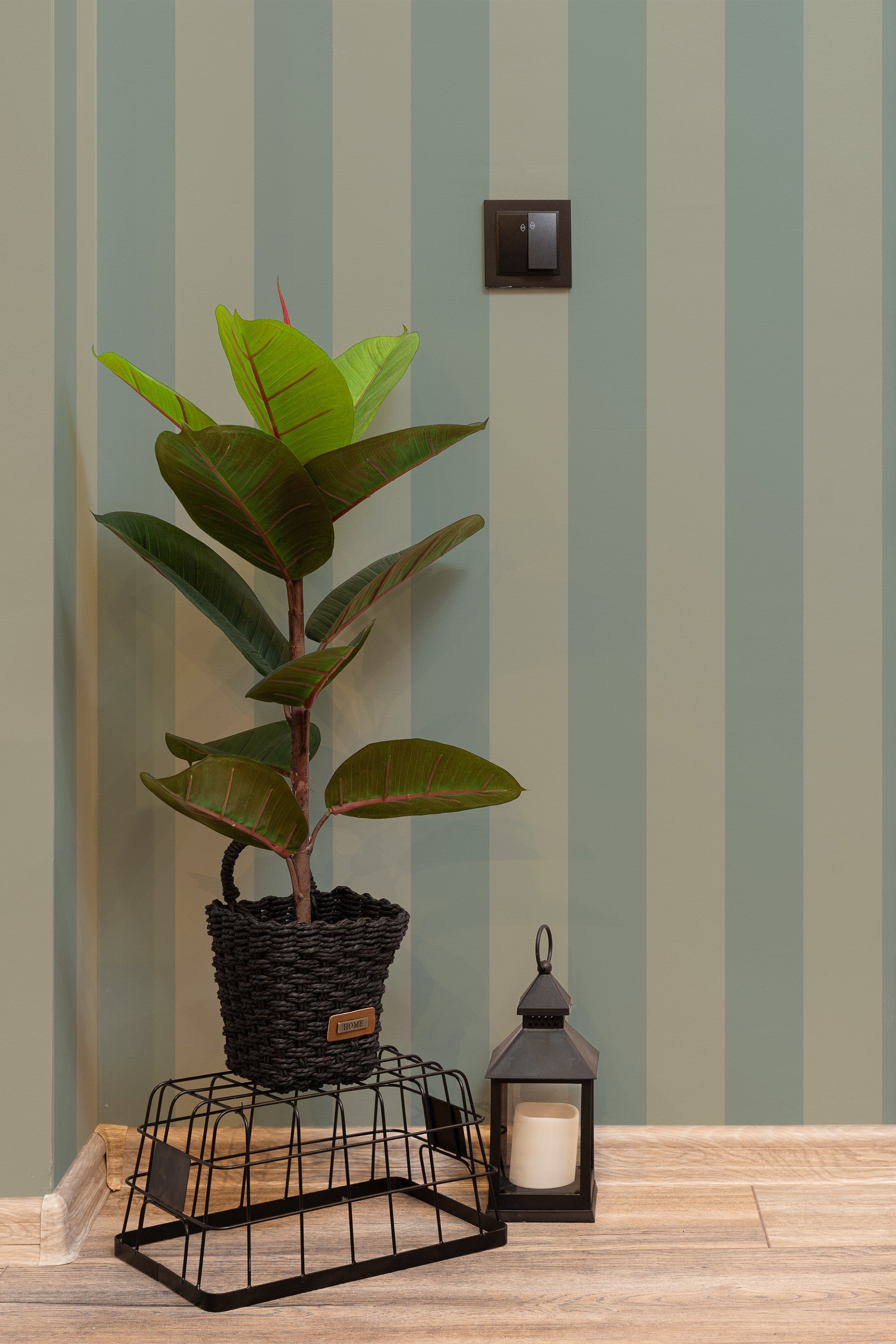 Self-adhesive wallpaper with alternating wide green and light stripes on a wall, complementing a potted plant and decor.