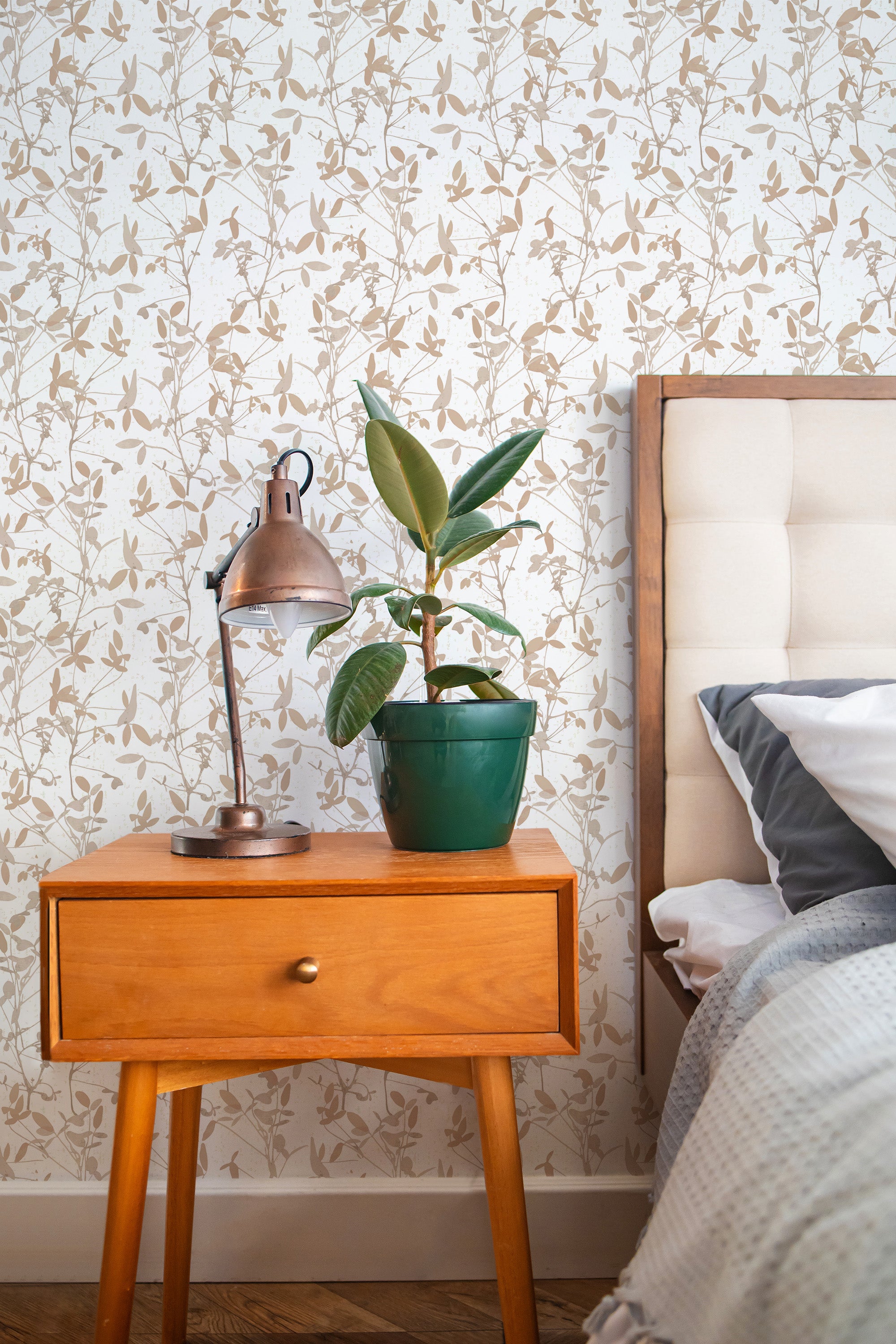 Self-adhesive wallpaper with a neutral floral pattern on a wall beside a wooden bedside table with a lamp and a plant.