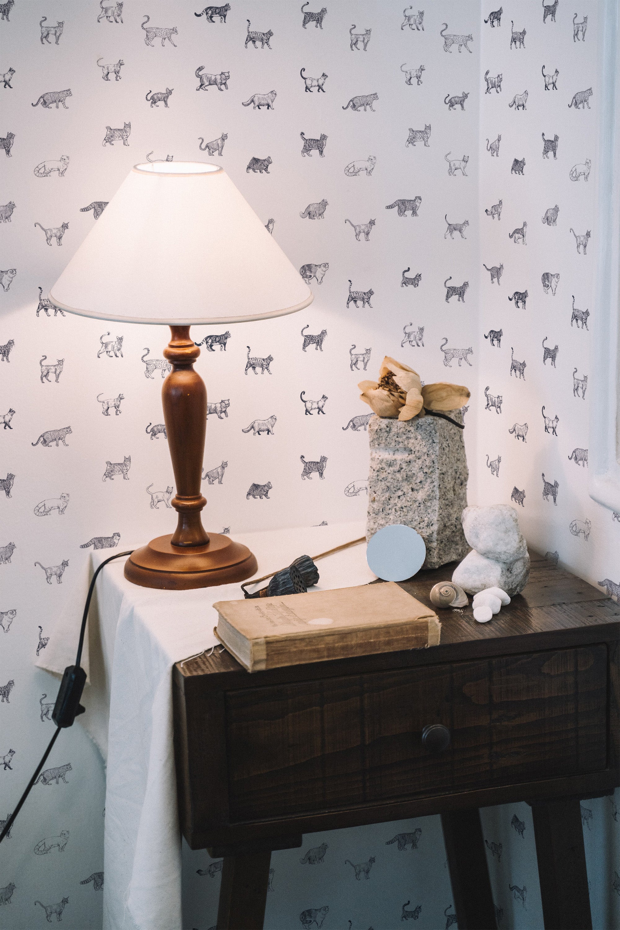 Self-adhesive wallpaper with repeated pattern of cat silhouettes on a plain background in a room with a wooden table and lamp.